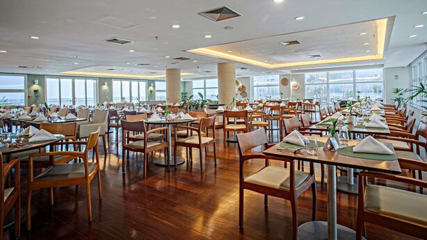 Un vaste espace dédié à la salle à manger, avec de nombreuses tables et chaises, de grandes fenêtres offrant une vue dégagée et un design moderne au niveau du plafond.