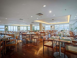 Un vaste espace dédié à la salle à manger, avec de nombreuses tables et chaises, de grandes fenêtres offrant une vue dégagée et un design moderne au niveau du plafond.
