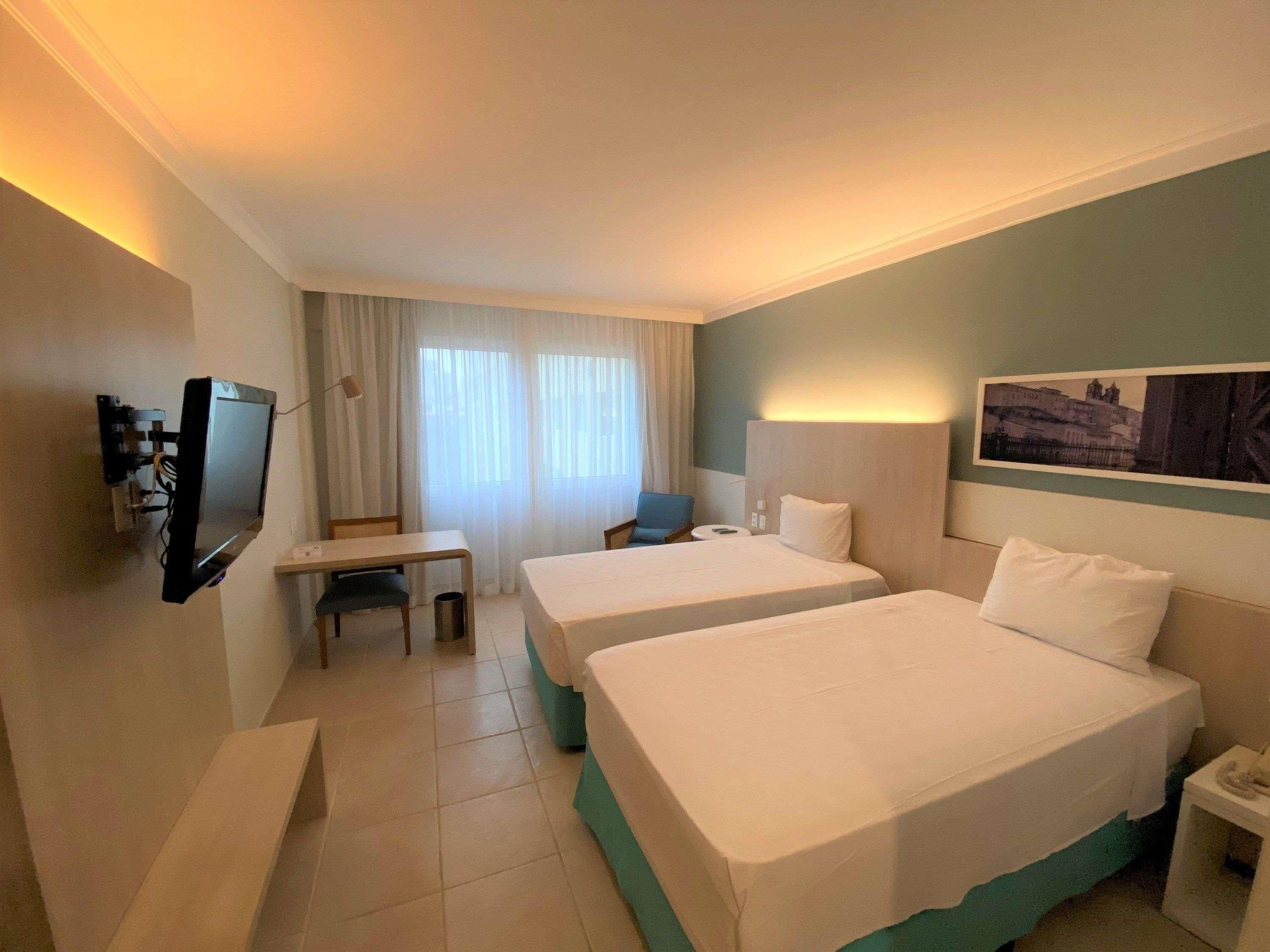 Een hotelkamer met twee bedden, een televisie, een bureau, een stoel en een raam met gordijnen.