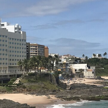 A coastal hotel with multiple floors, a beach in the foreground, and palm trees.