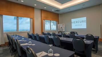 Uma sala de conferência com mesas, cadeiras e uma tela de projeção exibindo 'Mercure Hotels'.
