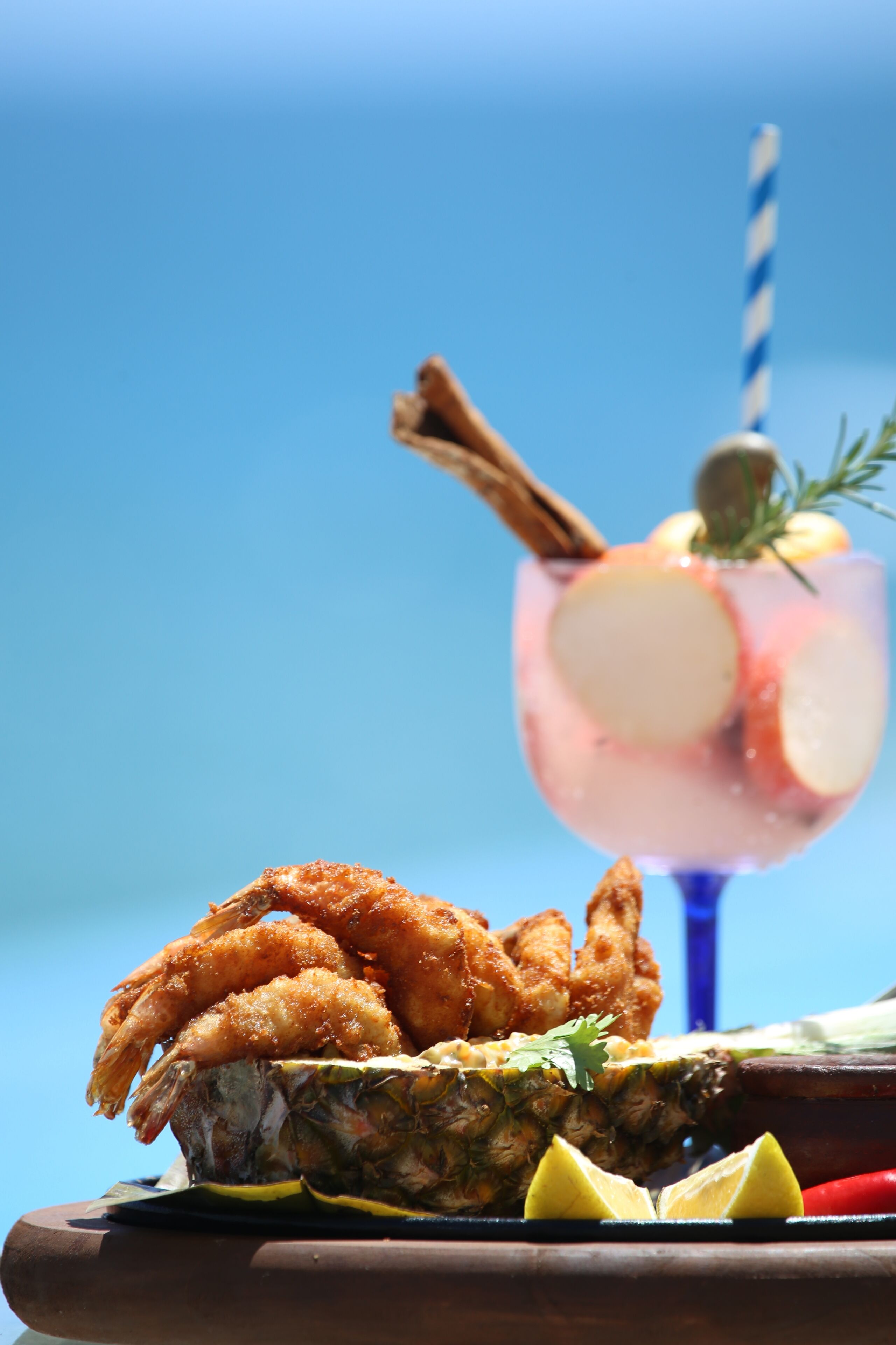 Una mesa de madera con mariscos fritos, una piña y una bebida con pajita.