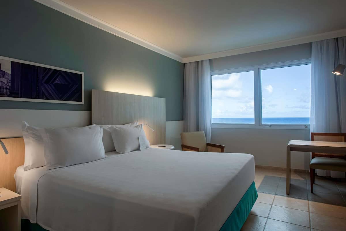 Ein Hotelzimmer mit Bett, Schreibtisch, Stuhl, Fenster mit Aussicht und einem Wandbild.