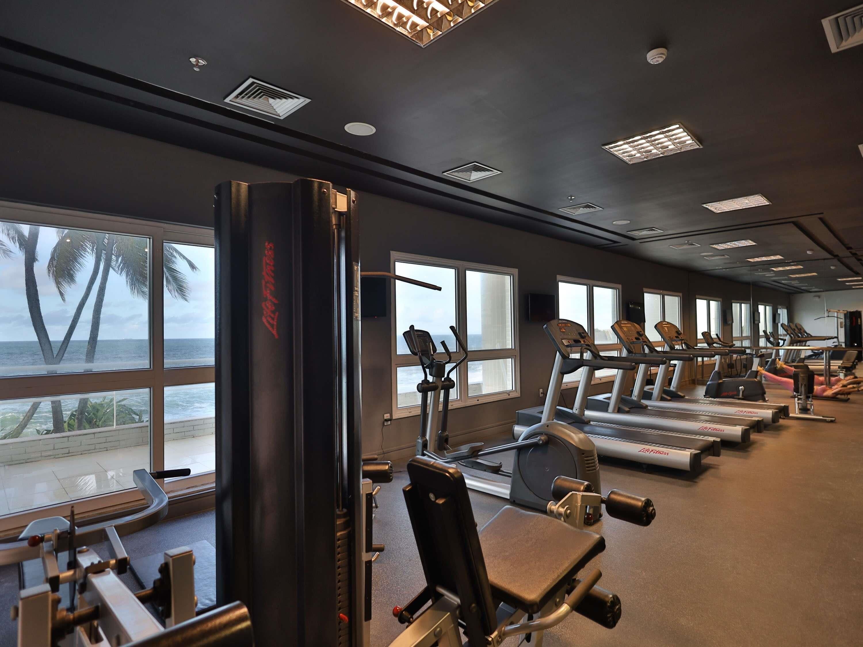 A gym with treadmills, weight machines, and large windows overlooking the ocean.
