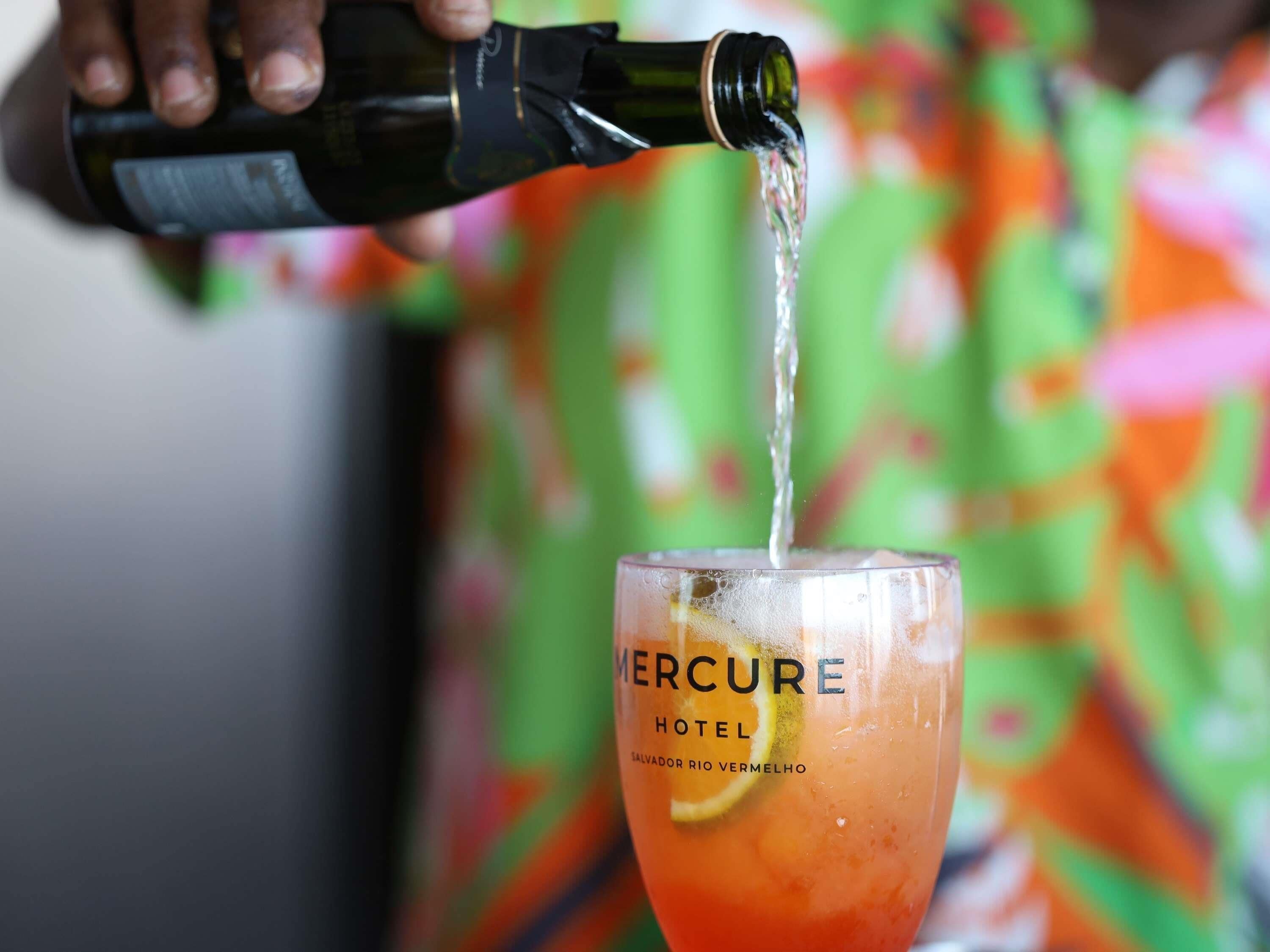 A hand pouring a drink into a glass labeled 'Mercure Hotel.'