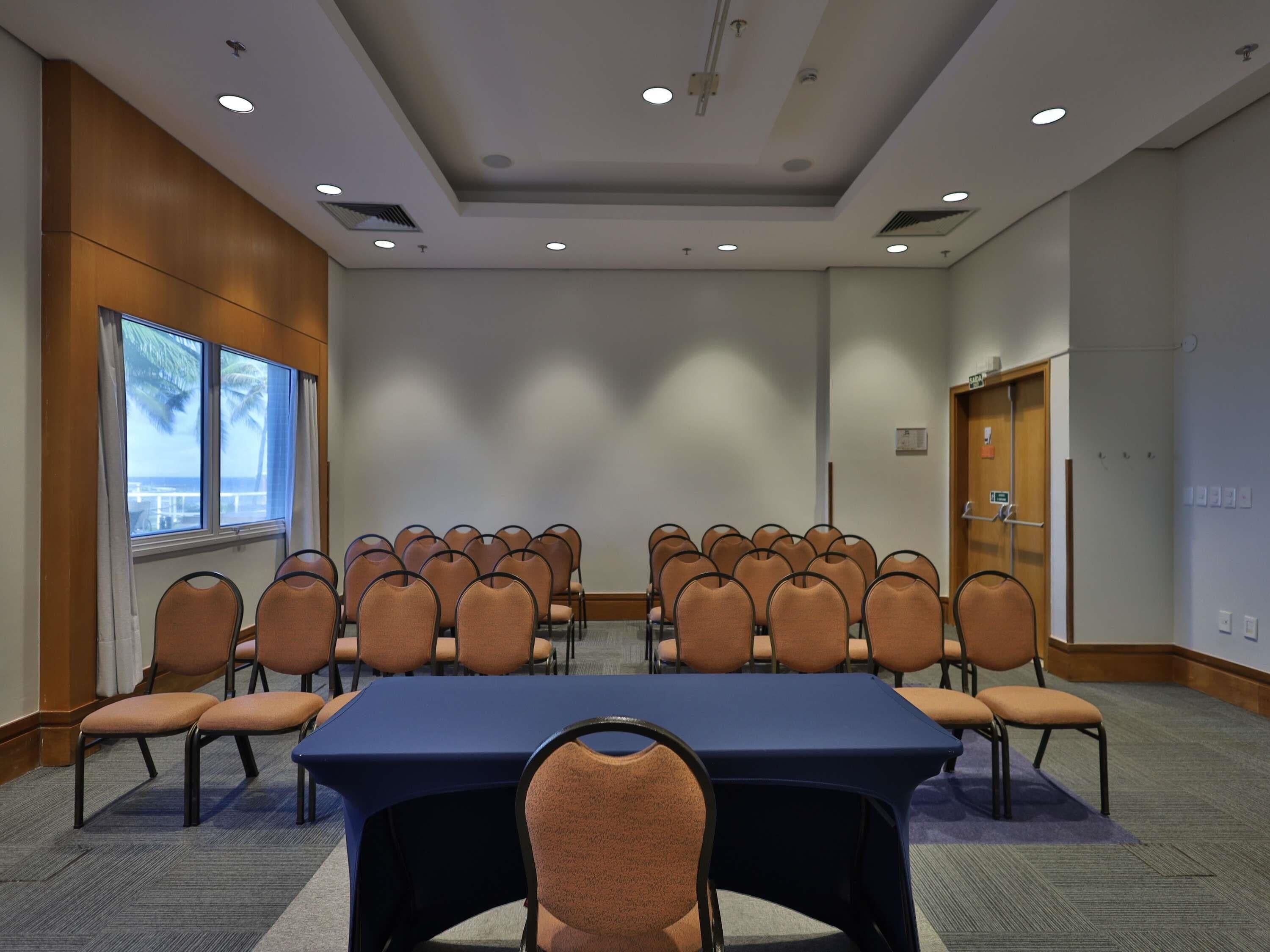 A conference room with a long table and chairs, large windows, and a door.