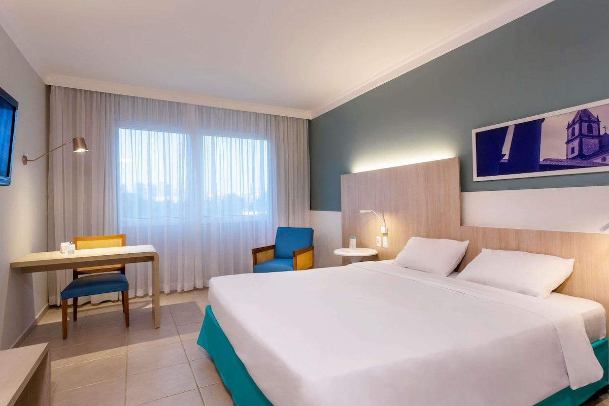 Une chambre d’hôtel équipée d’un lit, d’un bureau, d’une chaise, d’une petite table et d’une lampe fixée au mur.