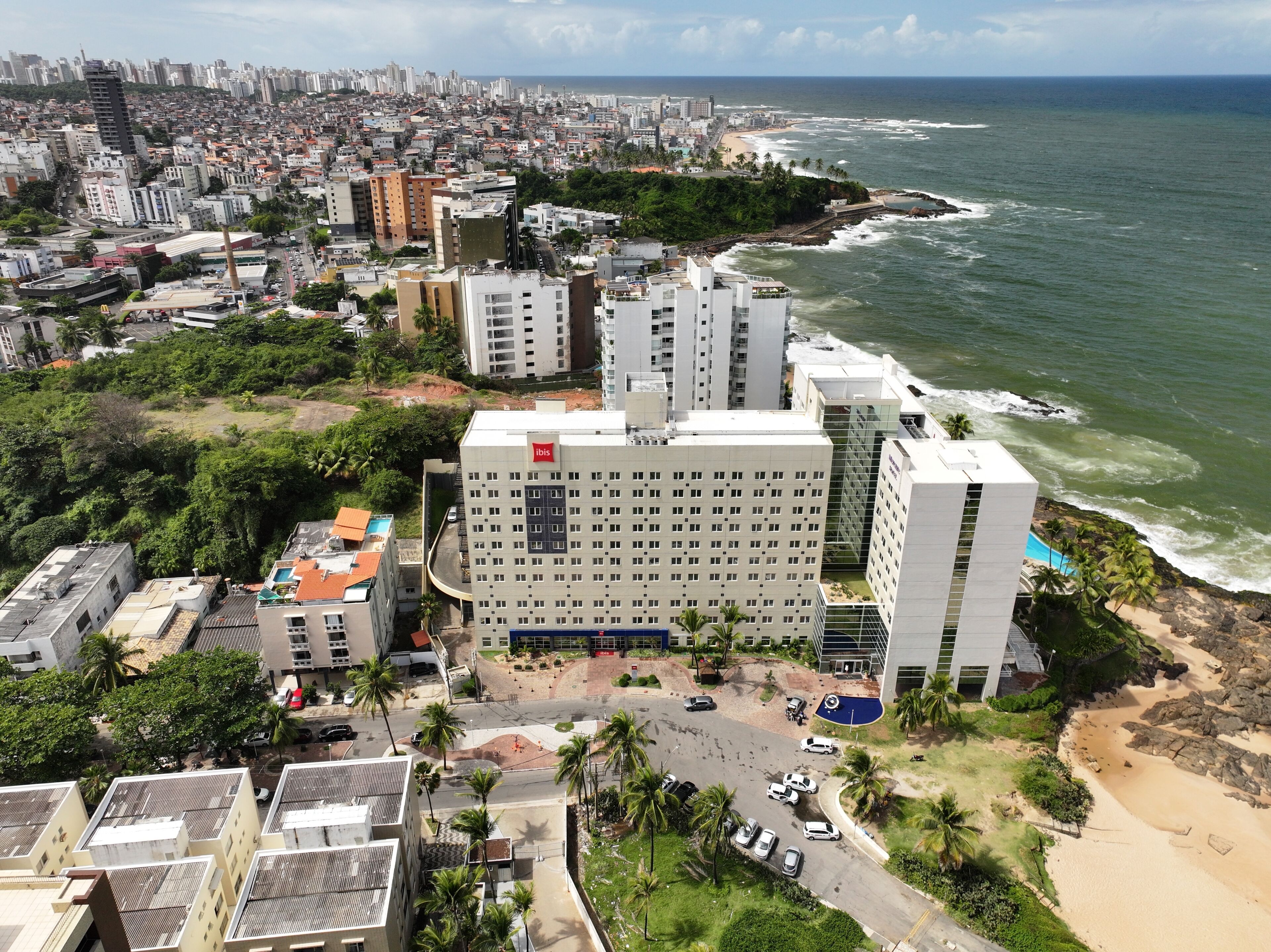 A coastal cityscape with a prominent hotel featuring a rooftop pool and a view of the ocean.