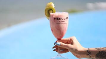 Una mano sostiene un vaso de cóctel rosa con una rodaja de kiwi, con la etiqueta 'Mercure Hotel' en Salvador, Río Vermelho.