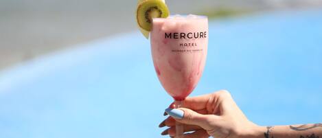 Eine Hand hält ein pinkfarbenes Cocktailglas mit einer Kiwischeibe, beschriftet mit 'Mercure Hotel' in Salvador Rio Vermelho.