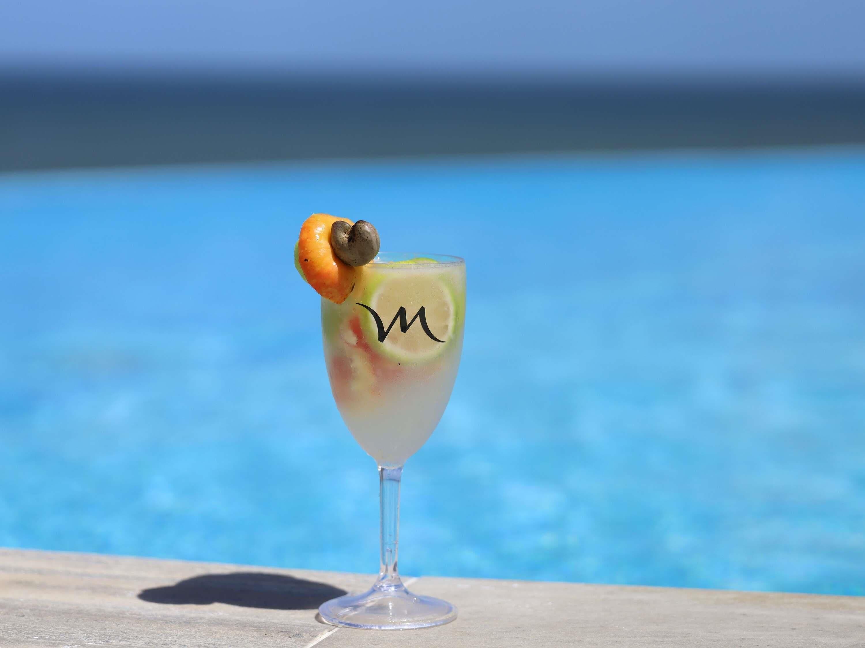 A cocktail glass with a lime slice and an orange garnish on a wooden surface by a pool.