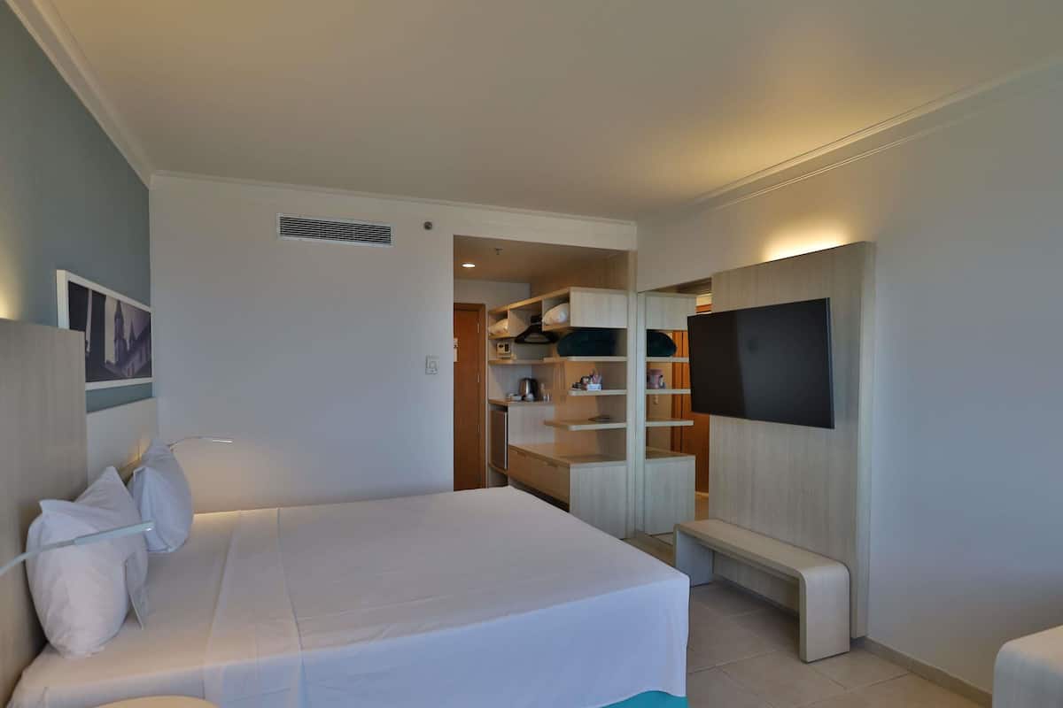 Ein Hotelzimmer mit Bett, Fernseher, Sitzbank und Küchenzeile.