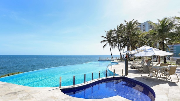 Une piscine avec vue sur la mer, des chaises longues et des parasols.