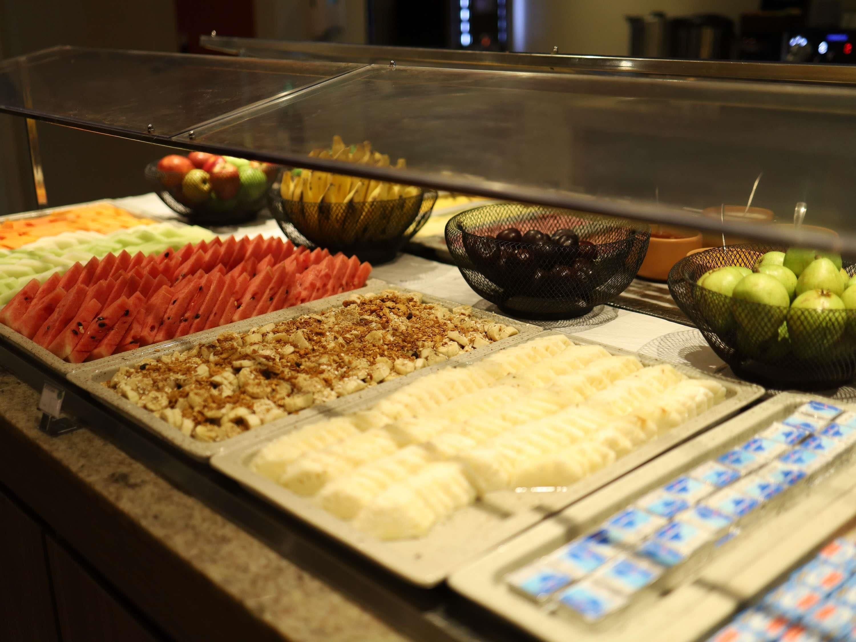 Buffet com diversas opções de comida, incluindo frutas fatiadas, castanhas e sobremesas.
