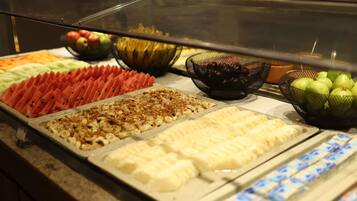 Buffet com diversas opções de comida, incluindo frutas fatiadas, castanhas e sobremesas.