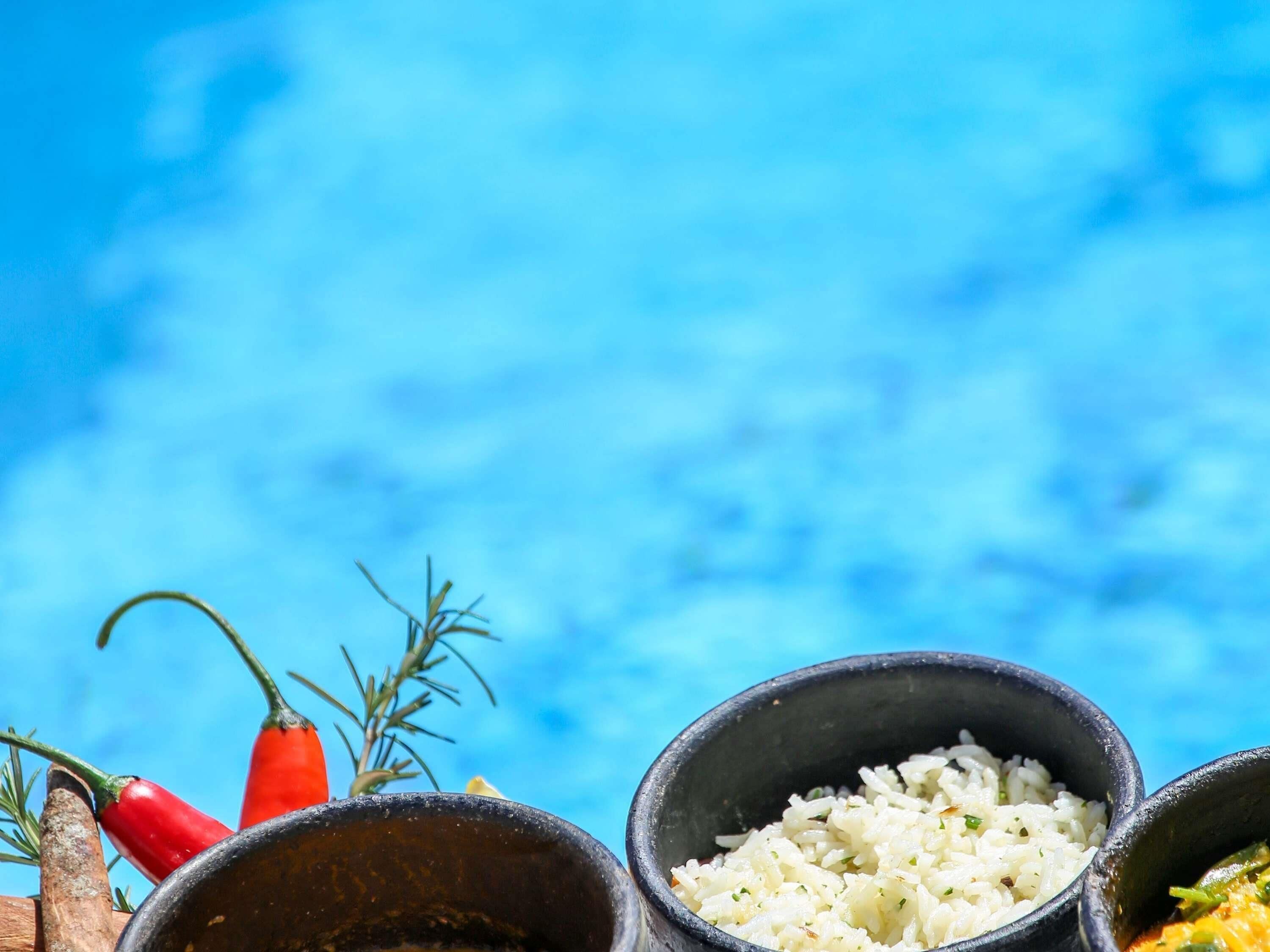 Céu azul e límpido com ambiente rústico, incluindo uma mesa de madeira, uma tigela de arroz branco e pimentas vermelhas.