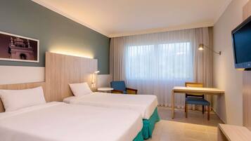 A hotel room with two beds, a desk, a chair, and a television.