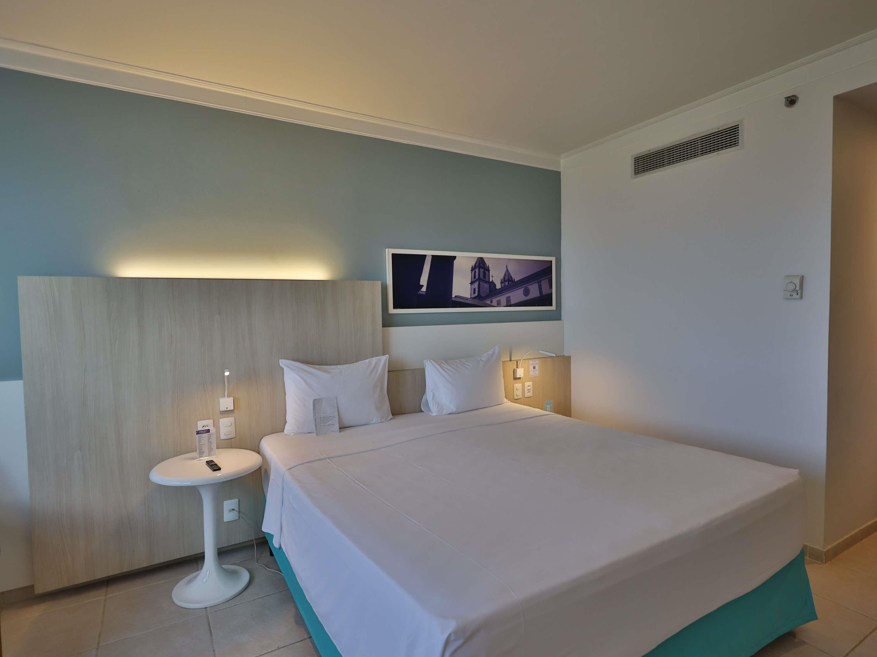 A hotel room with a bed, bedside table, and a wall-mounted picture.