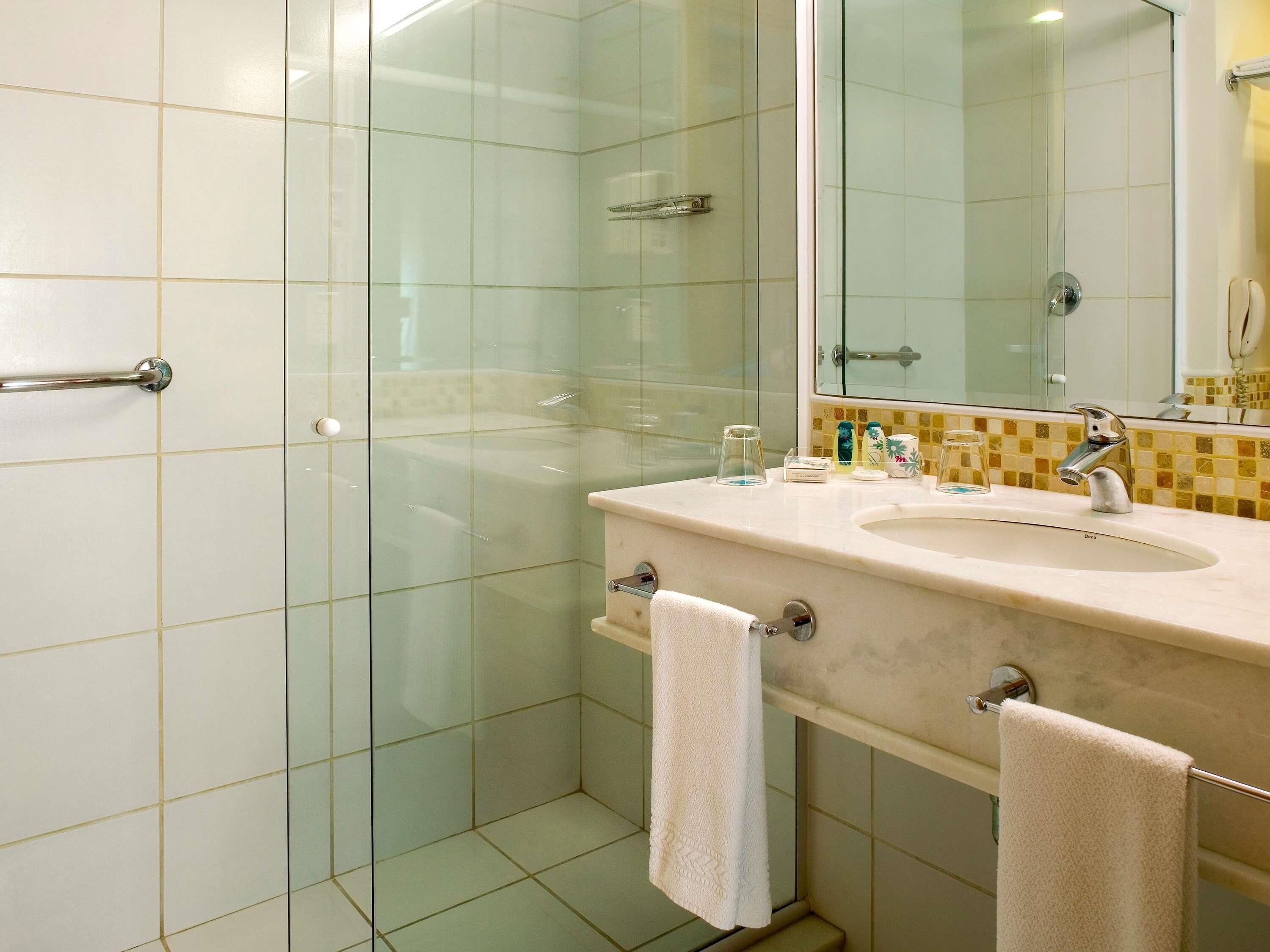 Een badkamer met een douchecabine van glas, een wastafel met spiegel, en twee handdoeken die aan een handdoekhouder hangen.