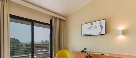 Une chambre d’hôtel avec un lit, un bureau, une chaise, une valise et une vue sur l’extérieur.