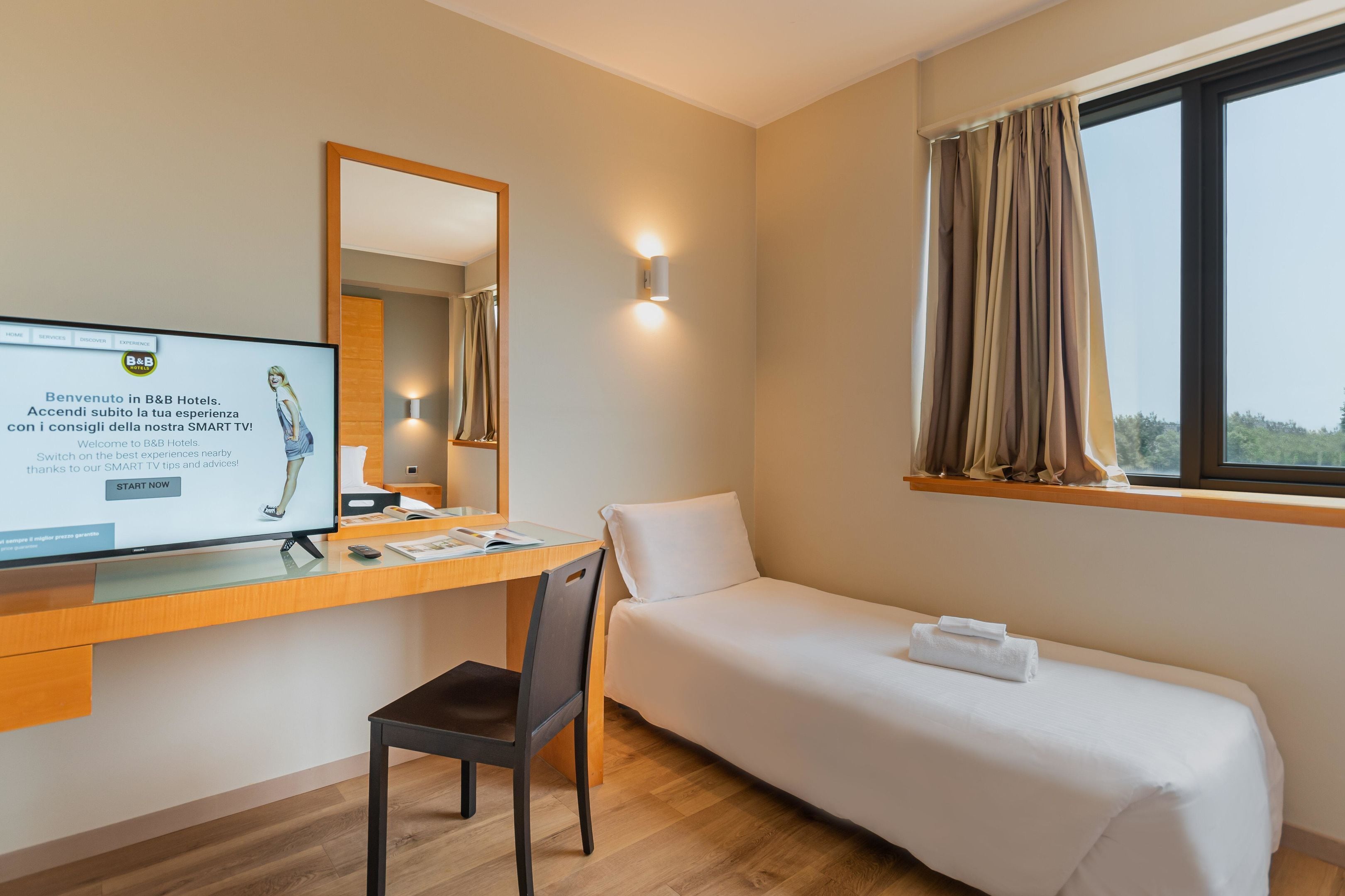 A hotel room with a desk, chair, bed, and a large window with curtains.