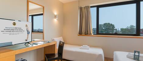 A hotel room with a desk, a chair, a bed, a small bedside table, a TV, and a window with curtains.