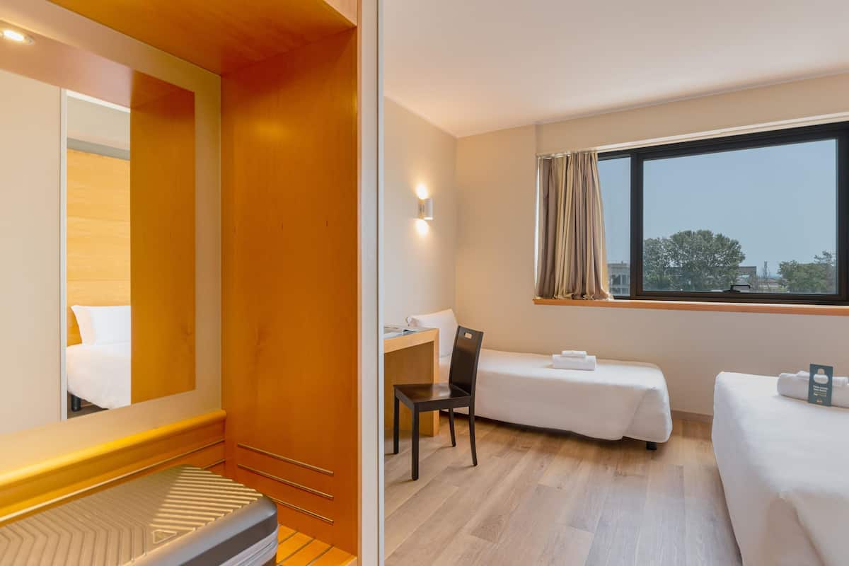 A hotel room with a bed, a desk, a chair, and a window with curtains.