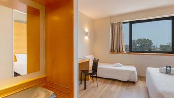 A hotel room with a bed, a desk, a chair, and a window with curtains.