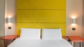A hotel room with a large bed, two bedside tables, and a bright yellow accent wall.