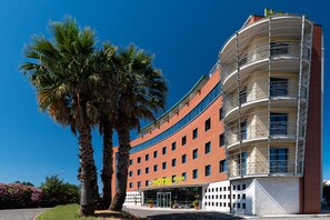 A modern hotel with a curved facade, multiple balconies, and a clear blue sky. - B&B HOTEL Pisa Airport (Pisa)