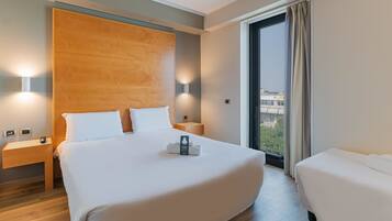 Ein Hotelzimmer mit einem großen Bett, einem kleineren Bett, einem Holz-Kopfteil, Nachttischlampen, einem Nachttisch und Blick auf die Stadt durch das Fenster.