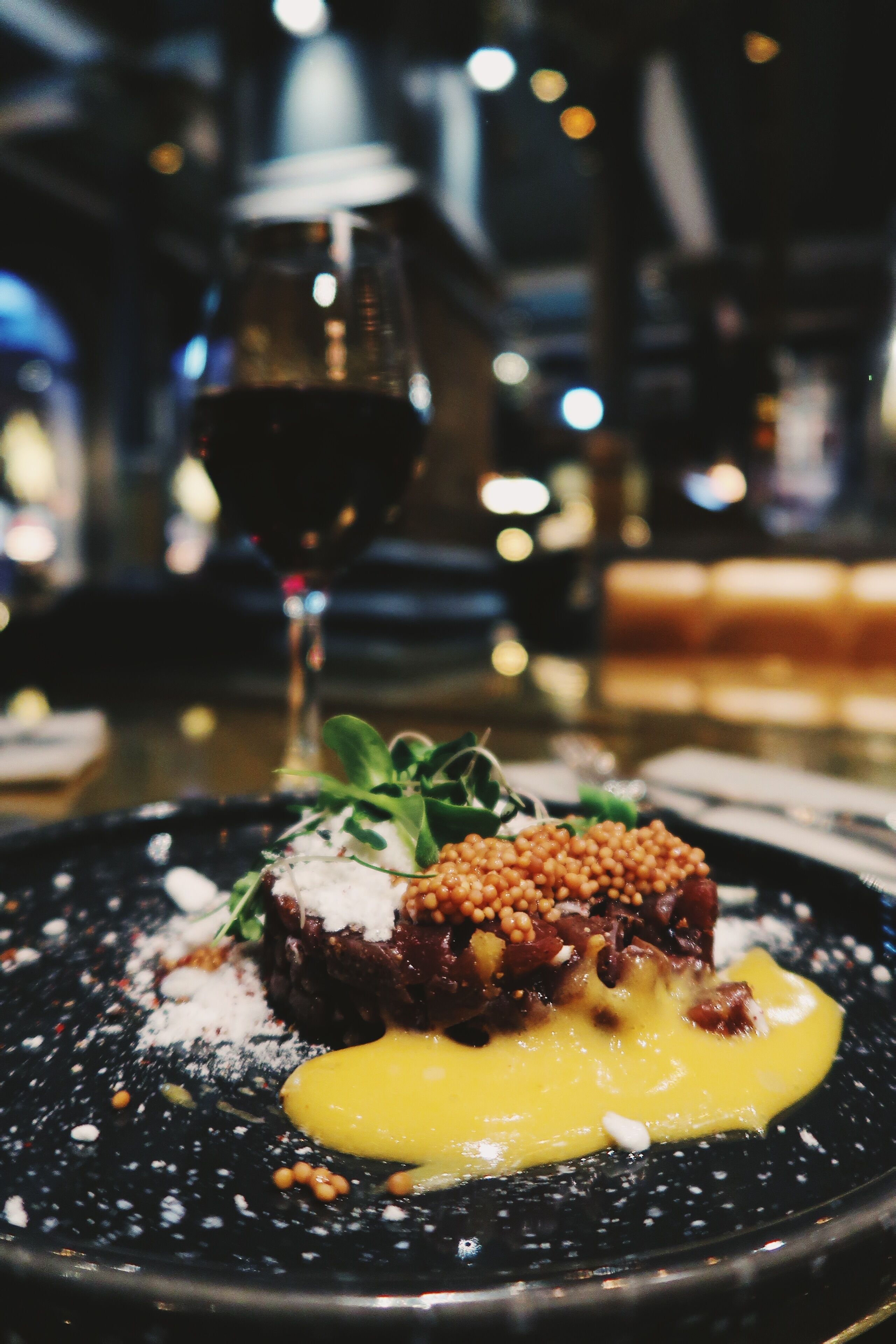 A close-up of a gourmet dish with a glass of red wine in the background.