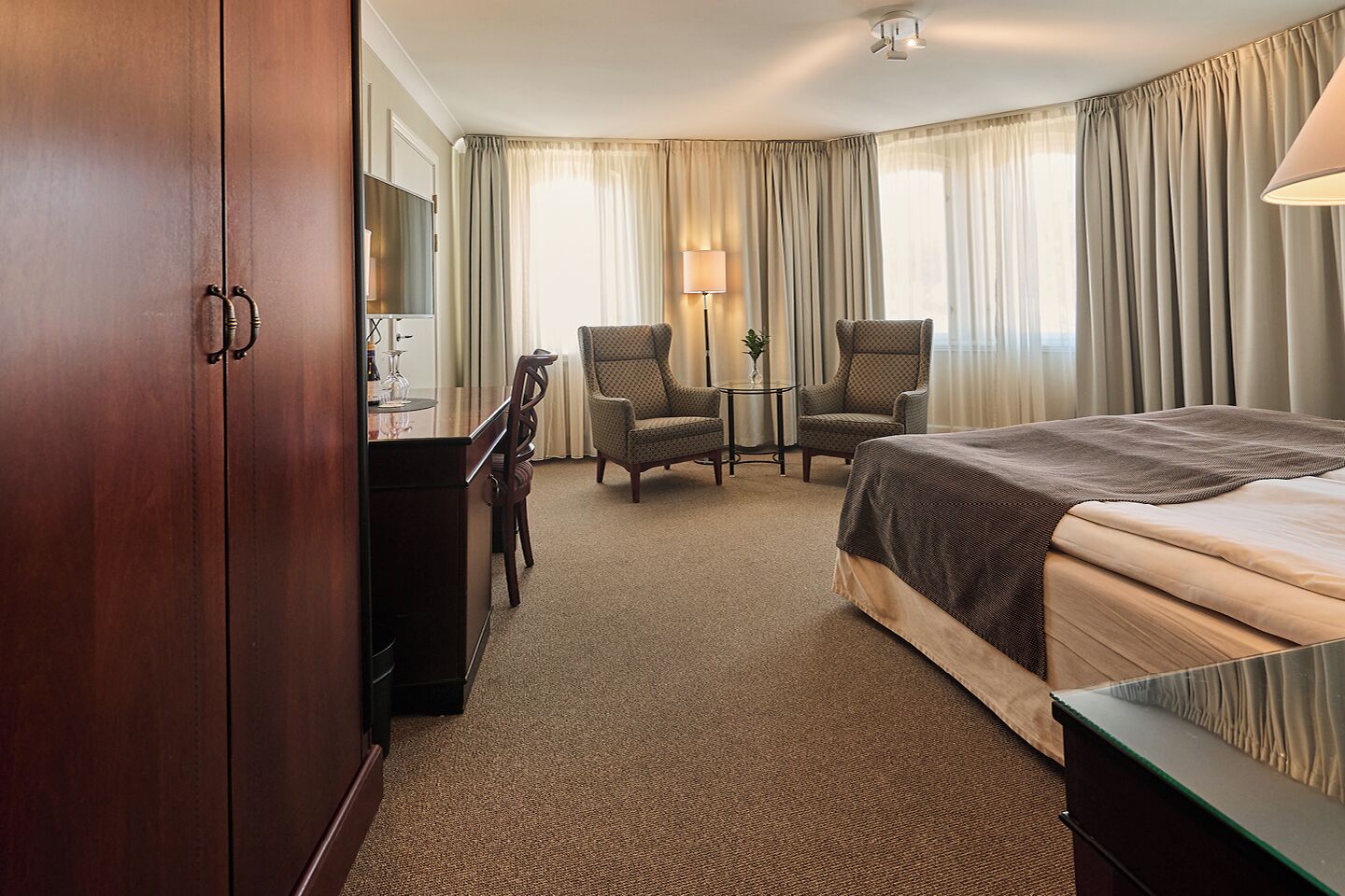 A hotel room with a bed, two armchairs, a desk, and a mirror.