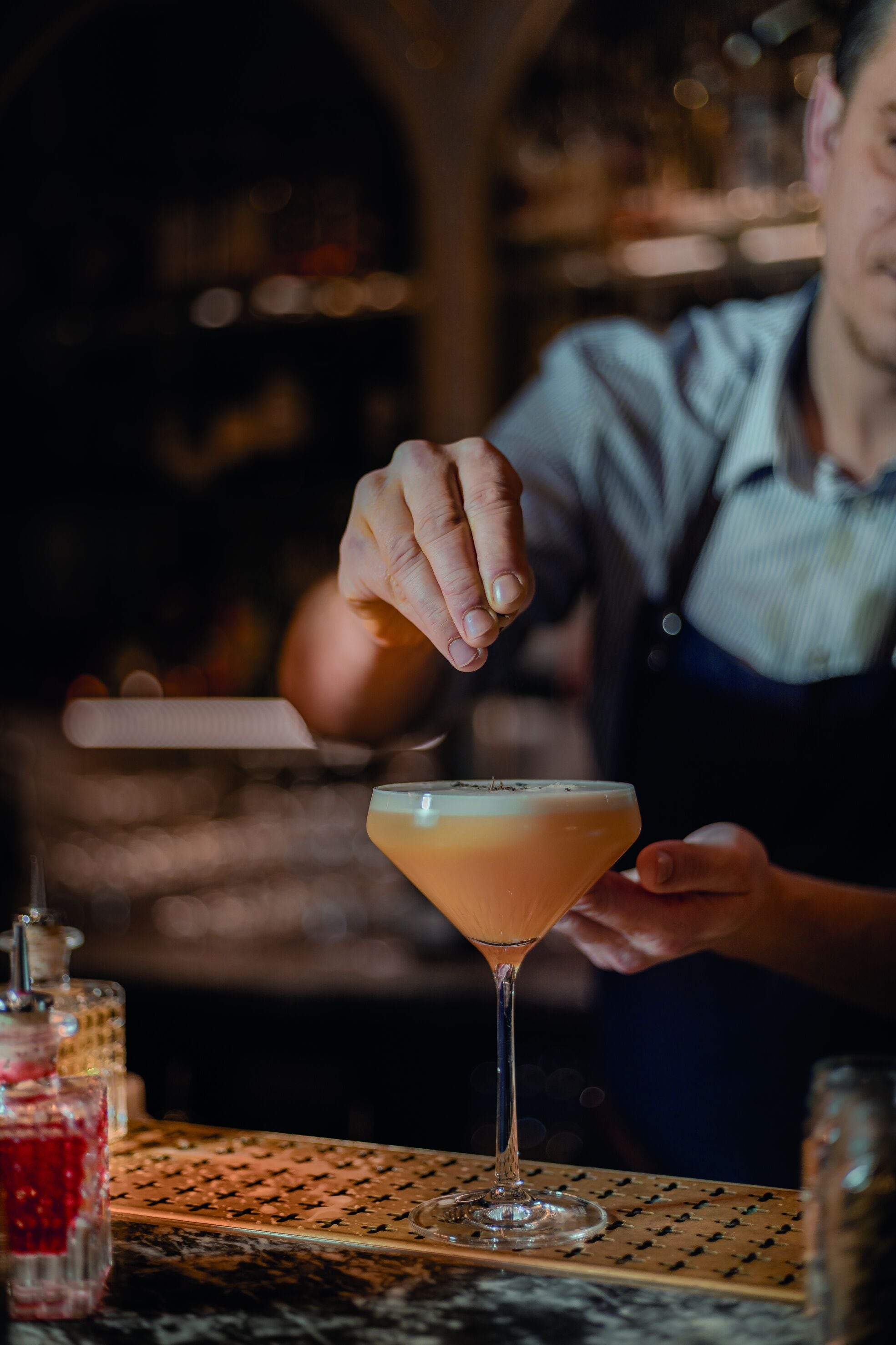 A bartender preparing a cocktail in a martini glass on a bar counter.