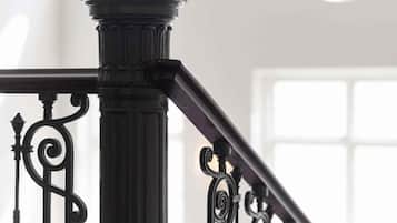 Una escalera con barandillas de metal negras y ornamentadas y una columna de estilo clásico.