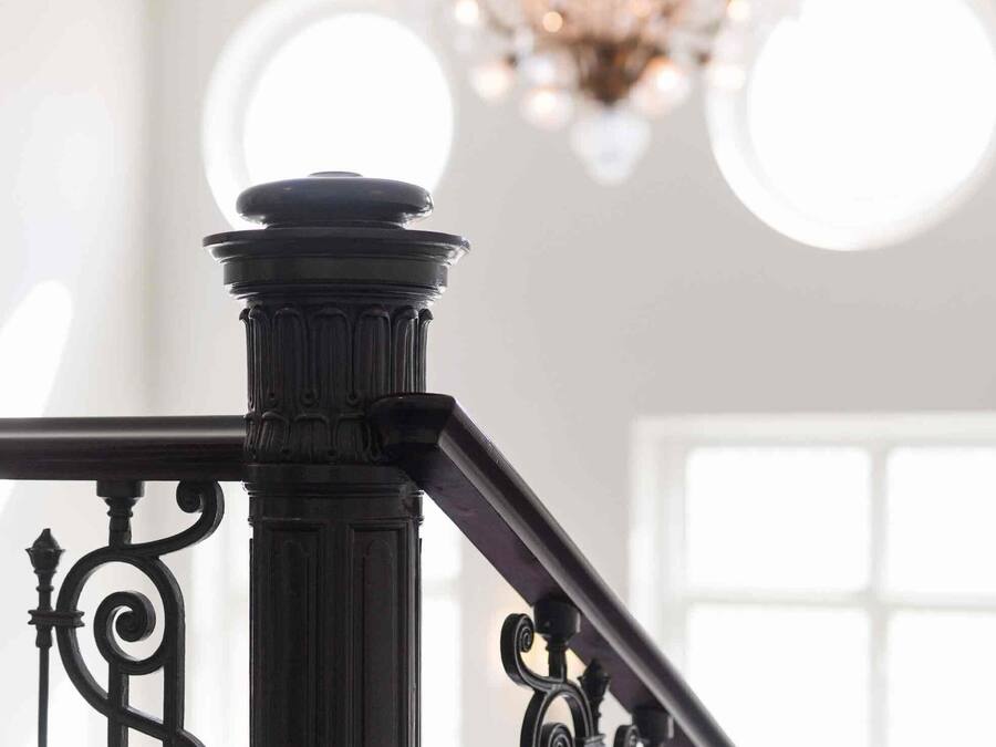 Una escalera con barandillas de metal negras y ornamentadas y una columna de estilo clásico.