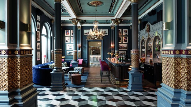 A grand lobby with a checkered floor, ornate columns, a chandelier, and a bar area.