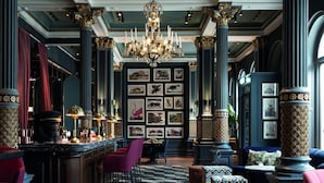 A luxurious bar area with a marble countertop, red bar stools, and a chandelier.