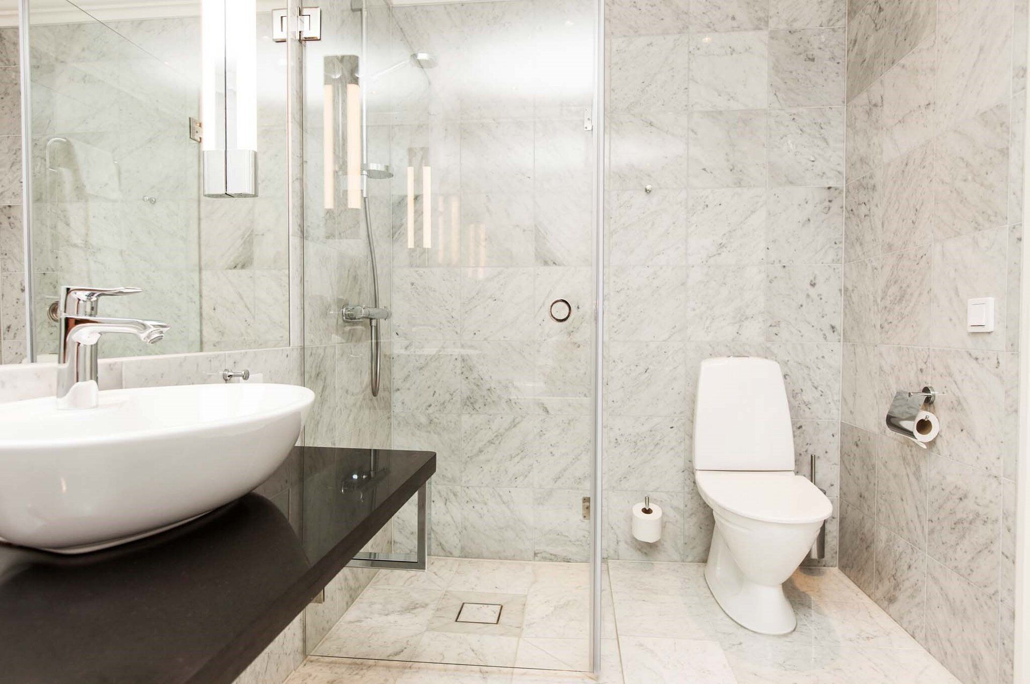 A modern bathroom with a large white sink, a glass shower enclosure, and a white toilet.