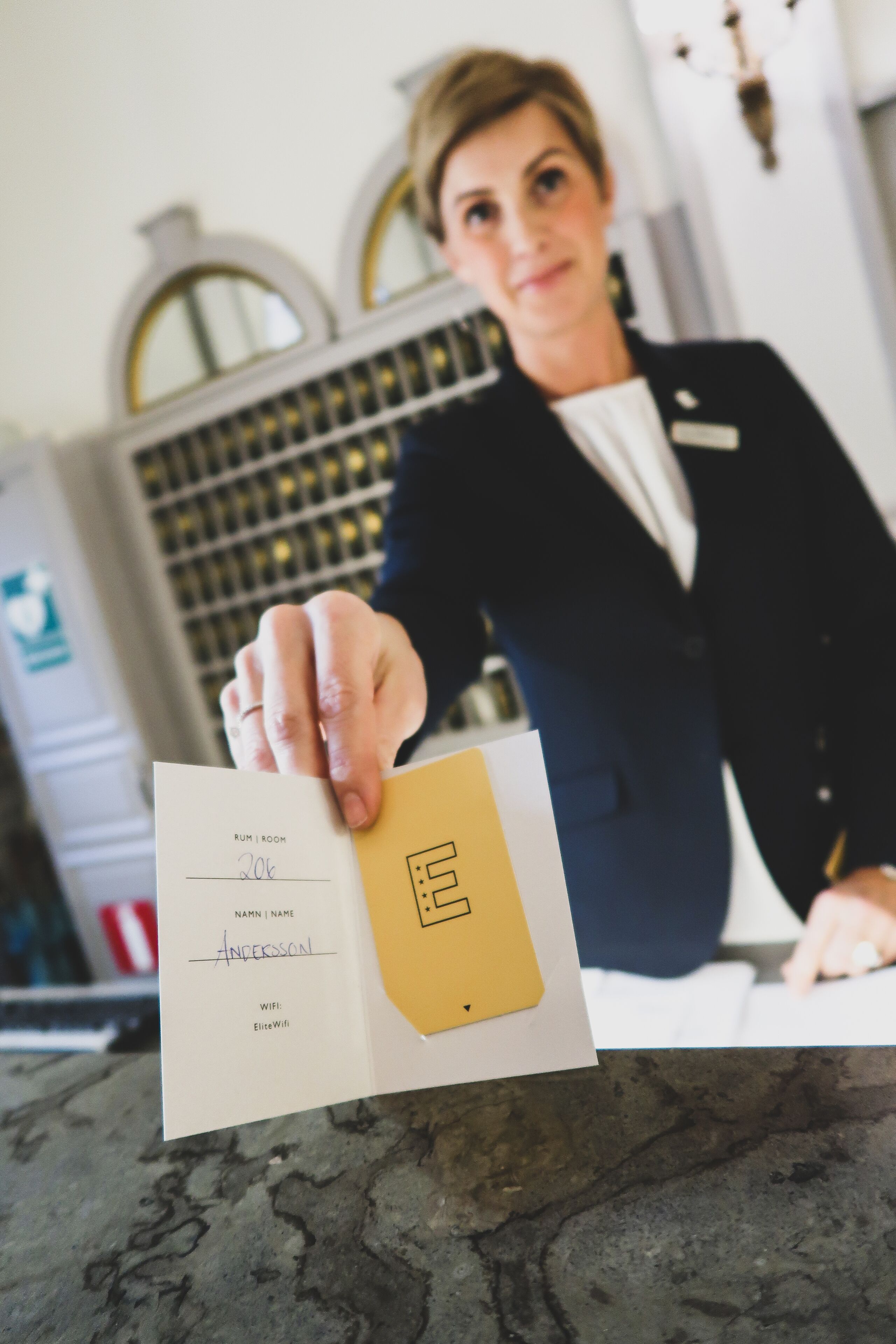 A person holding a room key card with a name and room number.