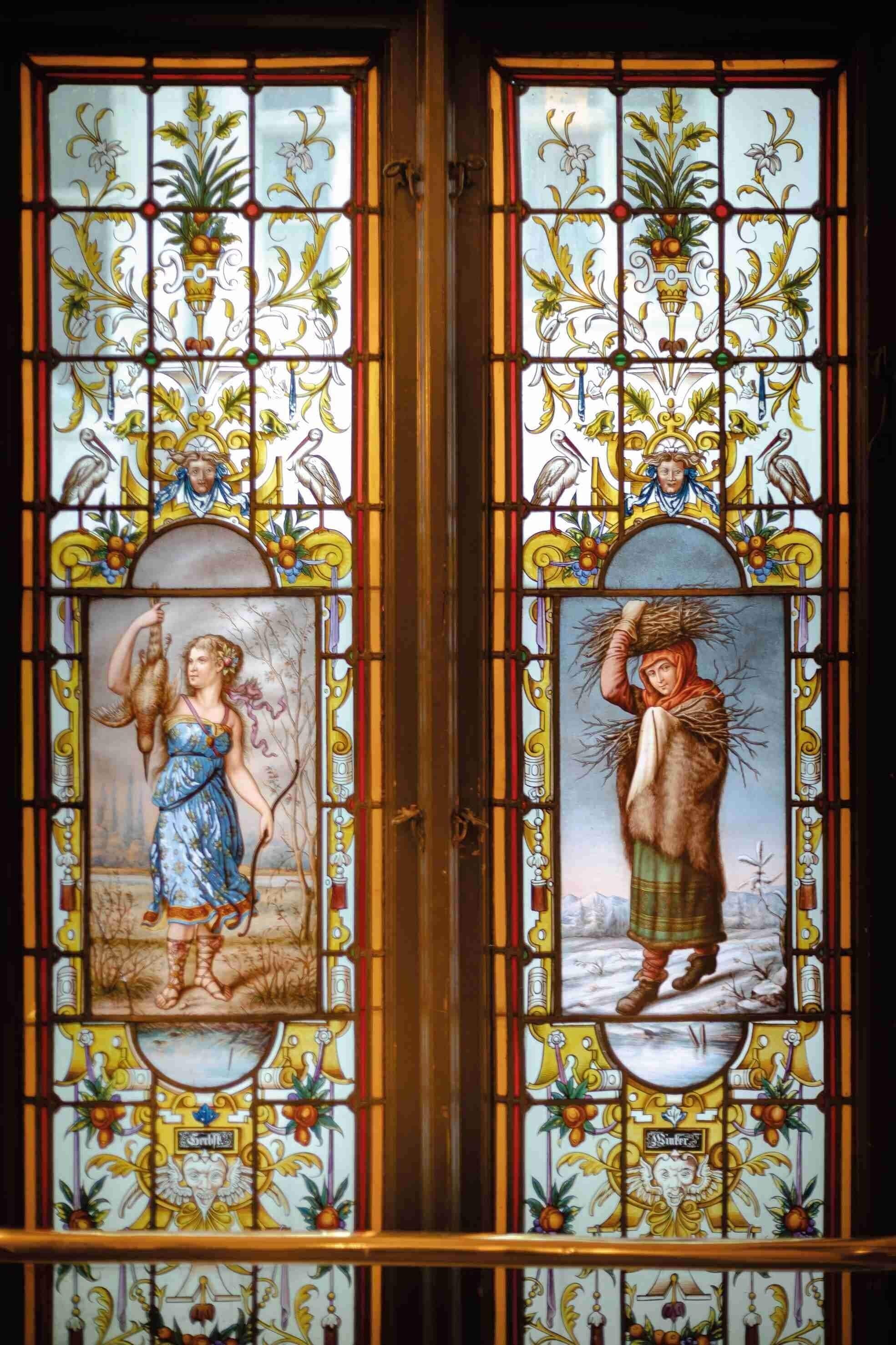 A stained glass window with two panels depicting figures, one holding a bird and the other carrying branches.