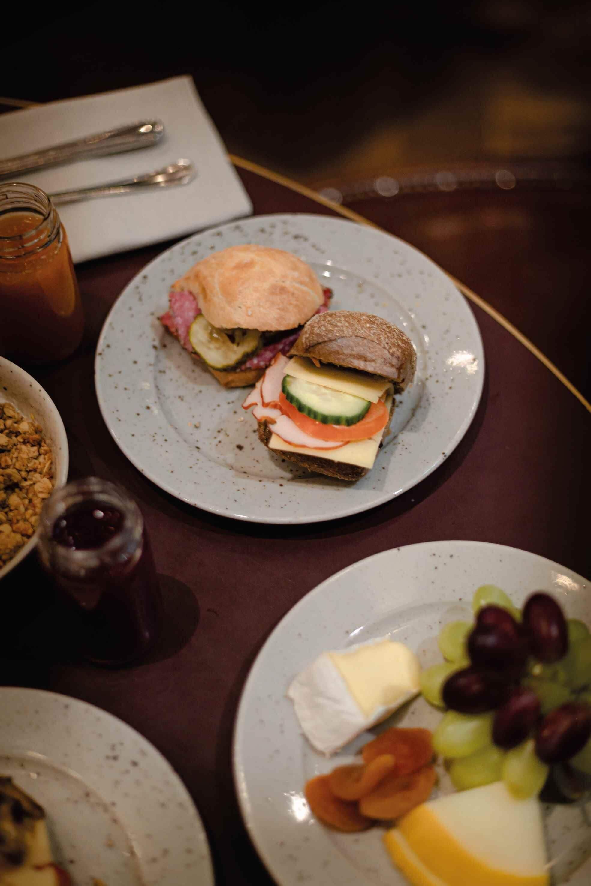 Una mesa de comedor con platos de comida, incluyendo un sándwich y una fuente de queso y uvas.