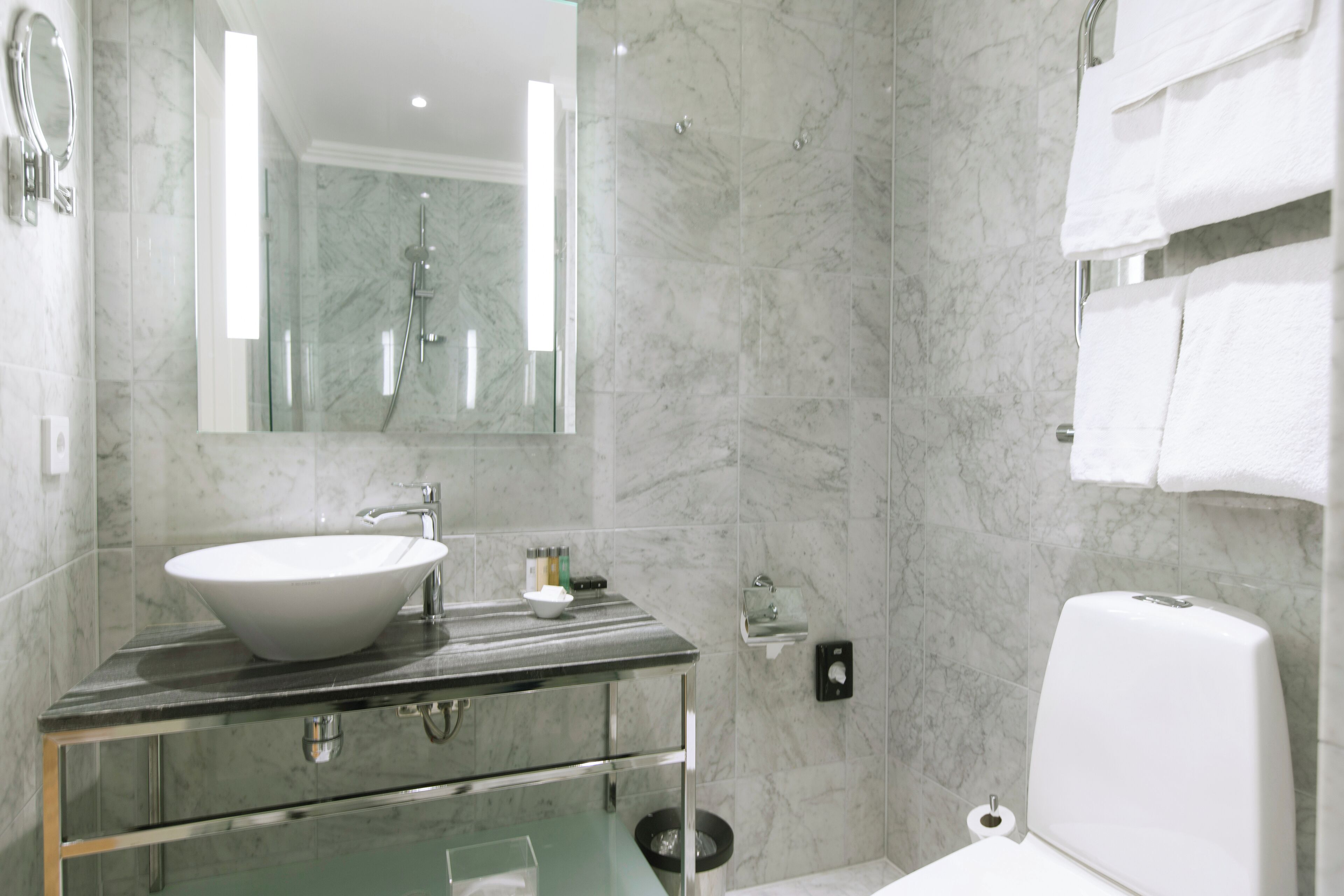 A modern bathroom with a marble sink, glass cabinet, and a toilet.