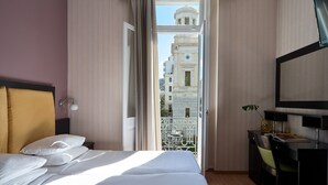 A hotel room with a bed, a desk, and a balcony with a view of a building. - Delphi Art Hotel (Athens)