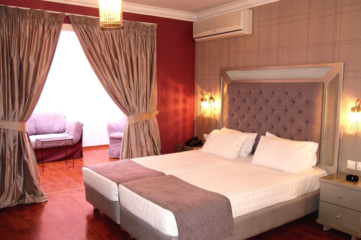 Une chambre d’hôtel avec un grand lit, une table de chevet, un appareil de climatisation, une chaise et des rideaux.