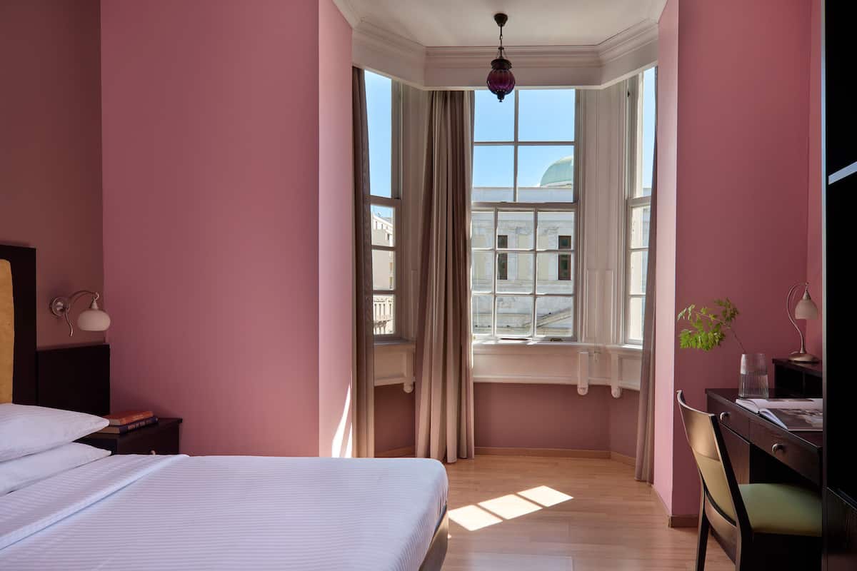 A bedroom with a bed, a desk, and a window with curtains.