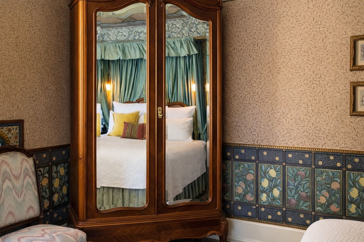 Una habitación con un armario de madera grande, una cama con cortinas verdes y una pared de azulejos con motivos florales.