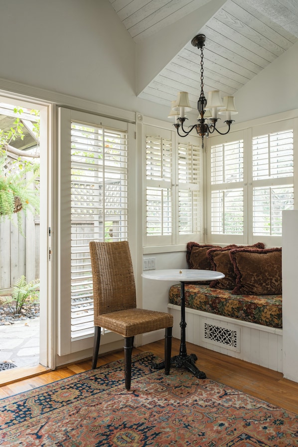 A room with a wicker chair, a small table, a bench with cushions, and a patterned rug. - Simpson House Inn (Santa Barbara)