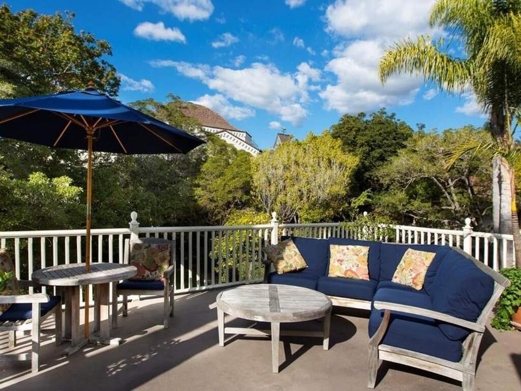 An outdoor patio with a blue umbrella, a round table, and a blue sofa with pillows.