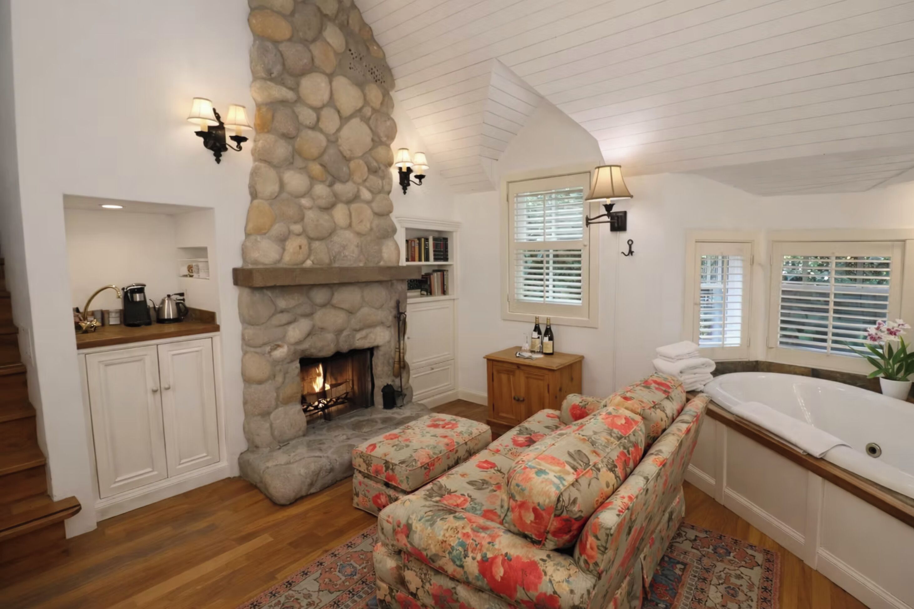 A cozy living room with a stone fireplace, a sofa, a coffee table, and a bathtub.